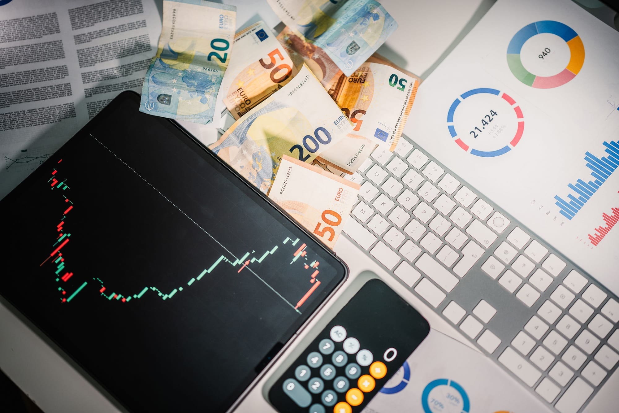Portátil con gráficos, billetes y una calculadora sobre el escritorio, en referencia a la Evaluación de Impacto (EIPD) de datos.