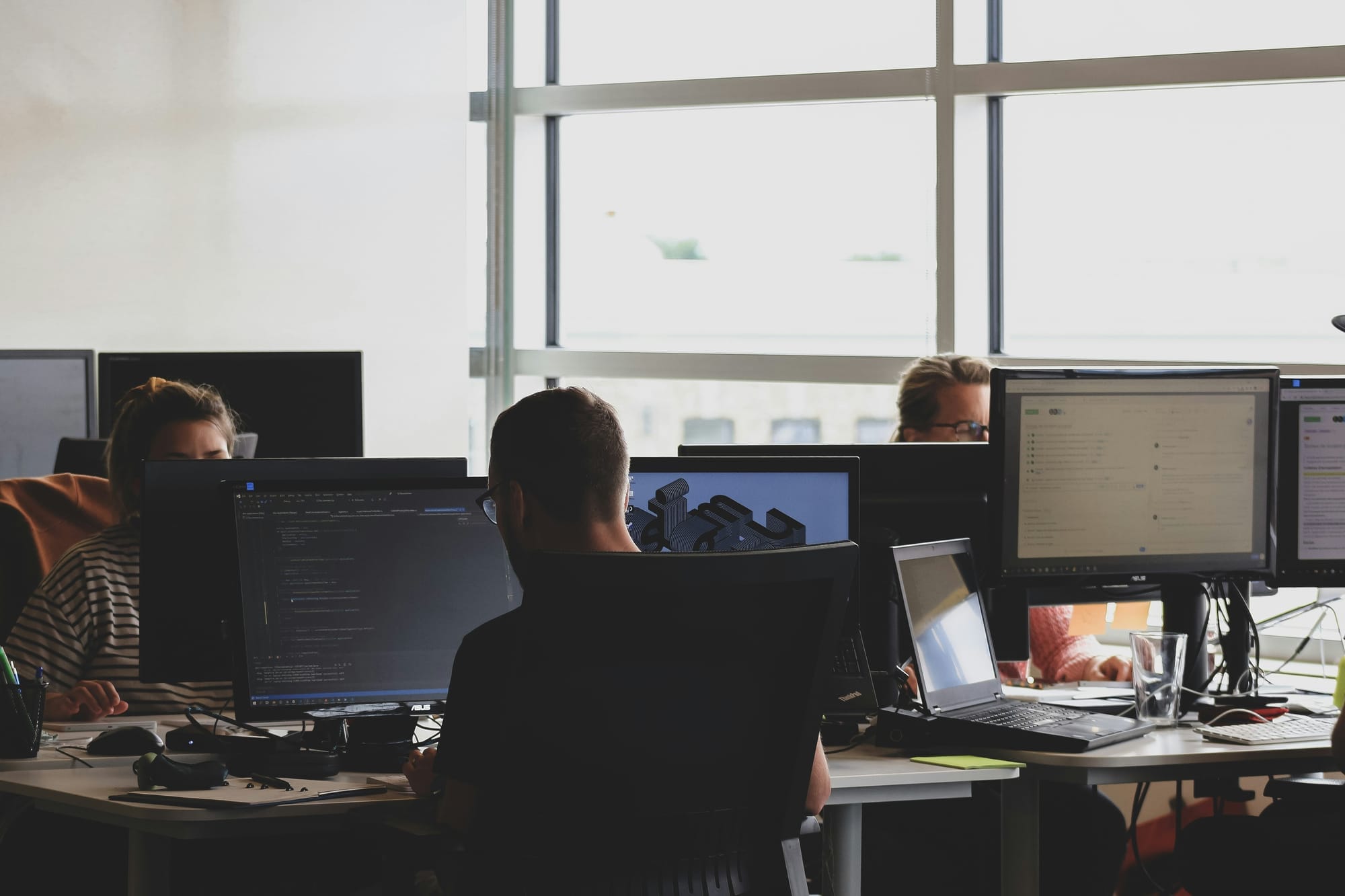 Personas en estaciones de trabajo con monitores, ilustrando que la Ley 21.719 de datos difiere de la de ciberseguridad.